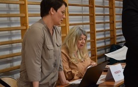 Sala gimnastyczna w Mszanie. Widok na stanowisko Urzędu Pracy. Dwie pracownice siedzą za stołem z dokumentami