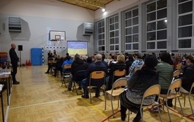 Sala gimnastyczna w Mszanie. Widok od tyłu na siedzące na krzesłach kilkadziesiąt os&oacute;b. Na wprost widoczny ekran z niebiesko-ż&oacute;łtą ukraińską flagą