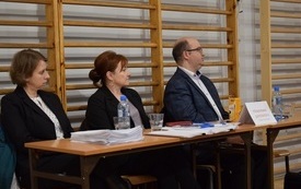 Sala gimnastyczna w Mszanie. Widok na stanowisko Ośrodka Pomocy Społecznej. Trzej pracownicy siedzą za stołem z dokumentami