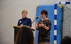 Sala gimnastyczna w Mszanie. Widok na m&oacute;wnicę i przemawiające dwie osoby - dyrektor urzędu pracy i tłumaczkę