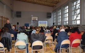 Sala gimnastyczna w Mszanie. Widok od tyłu na siedzące na krzesłach kilkadziesiąt os&oacute;b