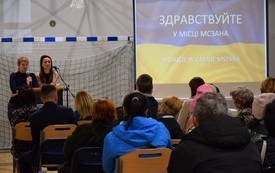 Sala gimnastyczna w Mszanie. Widok od tyłu na siedzące na krzesłach kilkadziesiąt os&oacute;b. Na wprost widoczny ekran z niebiesko-ż&oacute;łtą ukraińską flagą