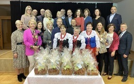 Sala Ośrodka Kultury w Połomi. Na pierwszym planie st&oacute;ł zastawiony zapakowanymi święcelnikami. Za nim stoją uczestnicy forum sekretarzy, pozując do wsp&oacute;lnego zdjęcia